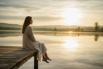 Peace doesn't feel empty. It only feels unfamiliar when chaos has felt like home. Woman sitting peacefully beside a calm lake representing nervous system healing, emotional safety, and learning to find peace after toxic relationships.